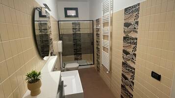 Ein Badezimmer mit weißem Waschbecken, einem Spiegel, einer Topfpflanze, einer Toilette und einer Duschkabine.