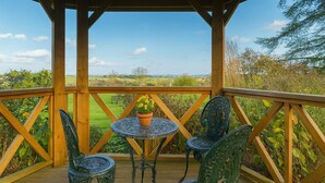 Une terrasse en bois avec une table et des chaises, donnant sur un paysage verdoyant.