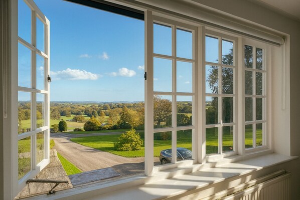 Blick aus einem Zimmer mit großen Fenstern auf eine ländliche Landschaft mit einer Straße und geparkten Autos.