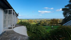 Une vue prise de l’extérieur d’un bâtiment, donnant sur un paysage verdoyant avec des arbres et un ciel dégagé.