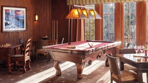 Une table de billard dans une pièce aux murs en bois et aux grandes fenêtres.