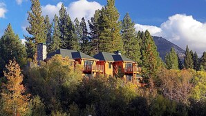 Un chalet à deux étages doté d’une cheminée en pierre, entouré d’une forêt dense et avec une montagne en toile de fond.