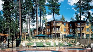 Un espace piscine avec des chaises longues et un bâtiment en bois doté de balcons.