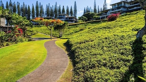 A pathway leading to a hillside with lush greenery and a row of modern buildings. - Kapalua Golf | Golf View 3 BR, Sleeps 12 | Car Incl. w/ 6+ Nights | KGV ML-2267 by KBM (Lahaina)