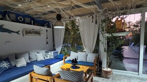 Un rincón exterior acogedor con temática náutica, que incluye un sofá, sillas de madera y una mesa.