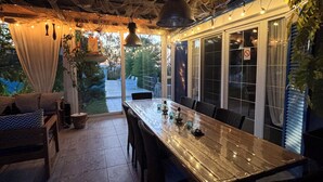 Un área de comedor al aire libre con una mesa larga, sillas e iluminación colgante.