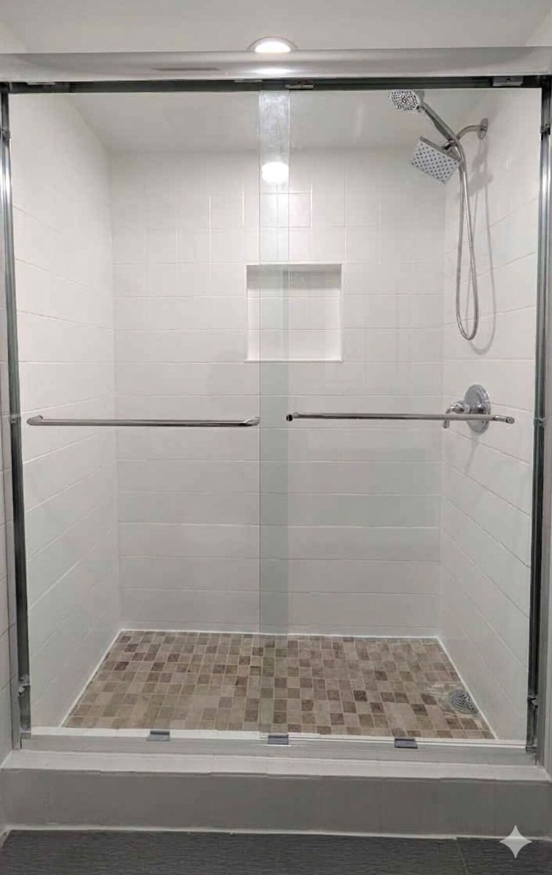A glass-enclosed shower with white tiled walls and a checkered floor.