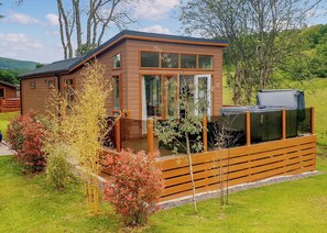 Eine moderne Holz-Blockhütte mit Terrasse, umgeben von üppiger Vegetation und Bäumen.