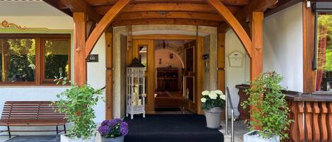 Entrada de un hotel con un arco de madera, una escalera con alfombra negra y plantas en macetas.