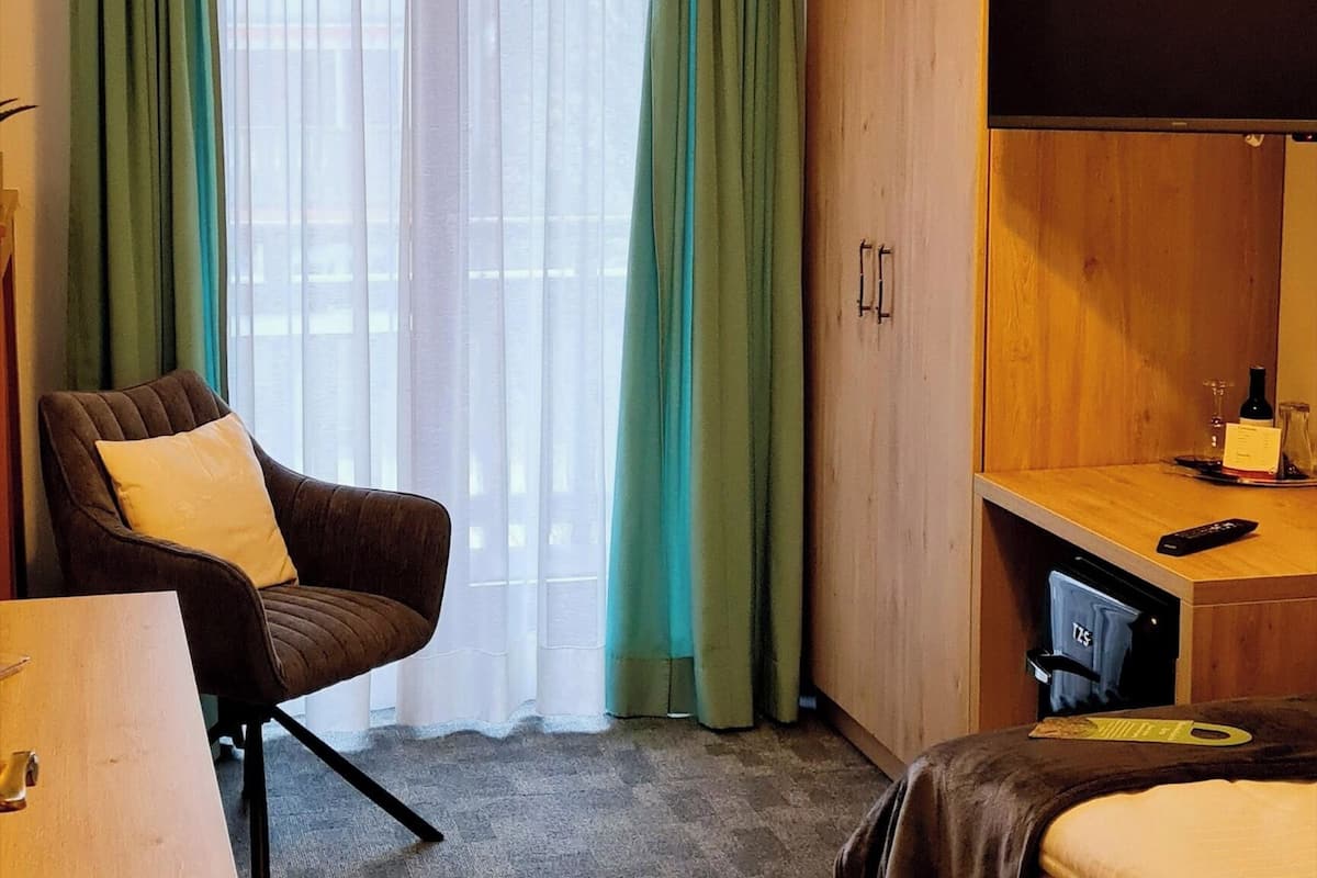 A hotel room with a bed, a desk, a chair, a television, and a window with curtains.