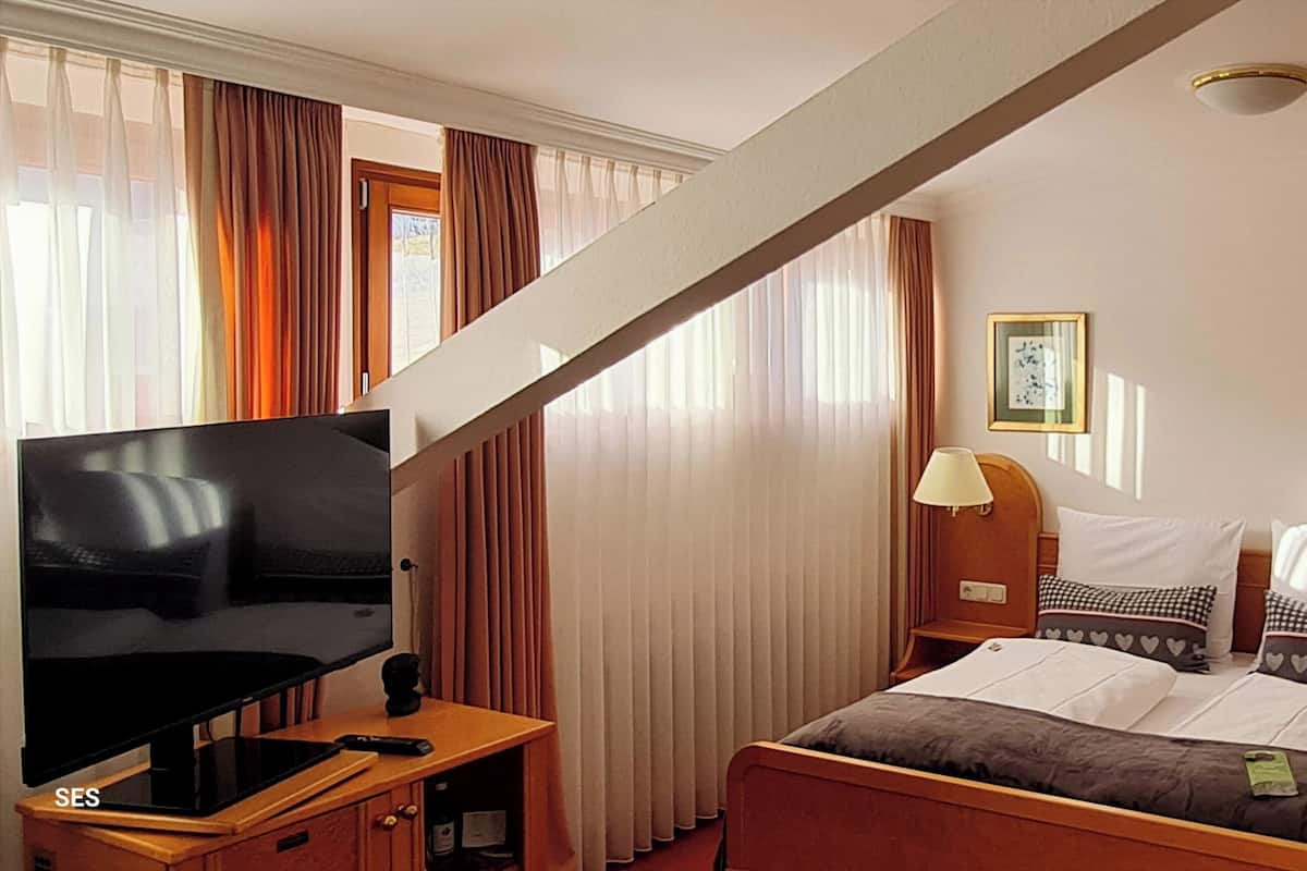 A hotel room with a bed, a TV, a bedside table, a lamp, and a picture on the wall.