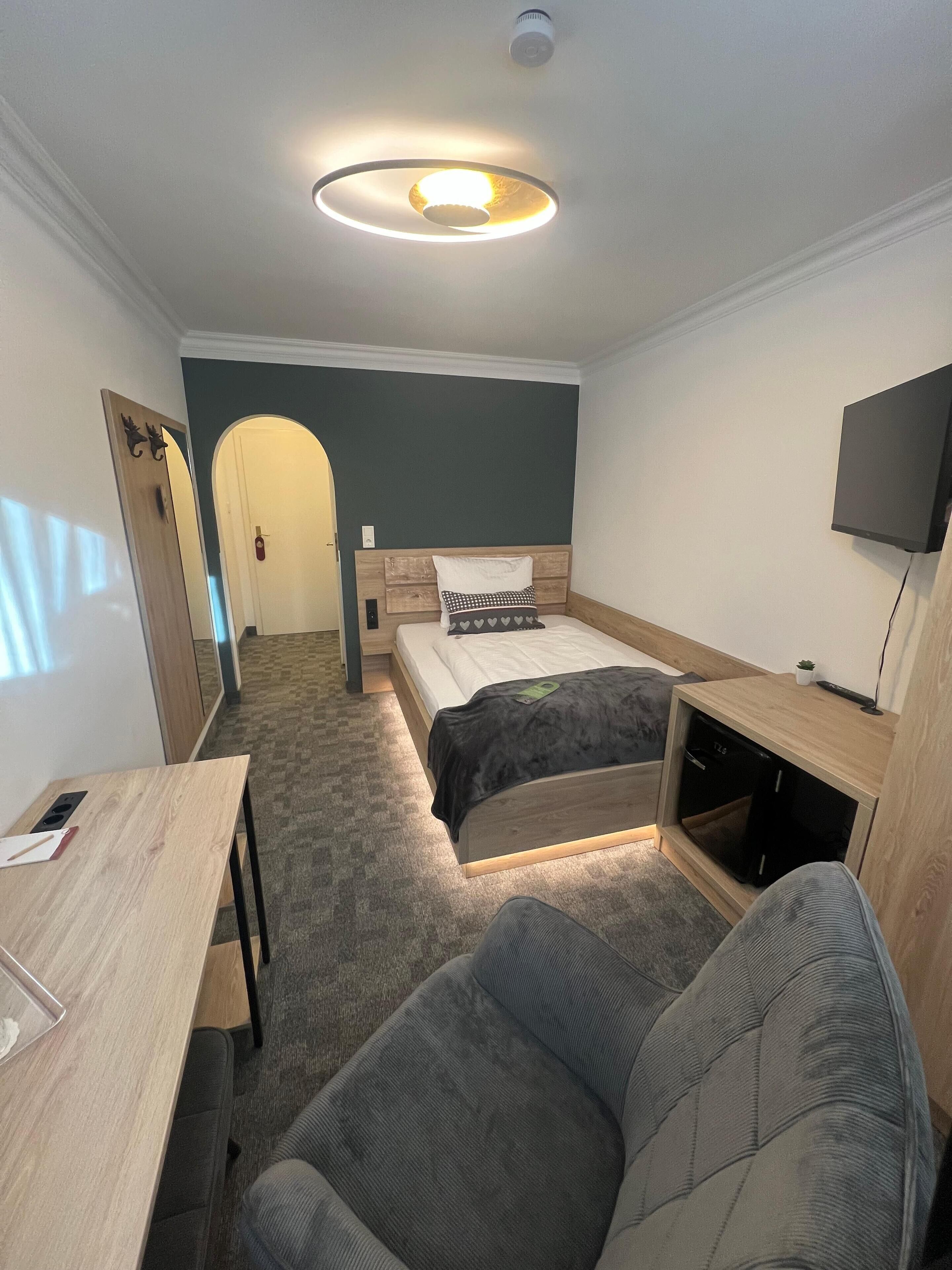 Une chambre d’hôtel équipée d’un lit, d’un bureau, d’une chaise, d’une télévision et d’un luminaire au plafond.