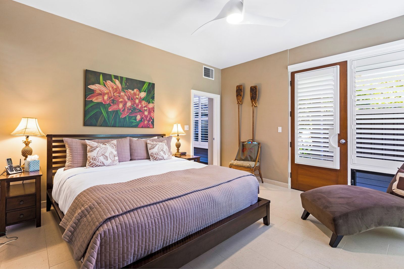 Et soveværelse med en stor seng, sengeborde med lamper, et maleri, en stol og en dør med persienner.