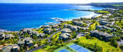 Vue aérienne d’un quartier résidentiel situé sur la côte, avec des maisons, un court de tennis et une vue sur l’océan.