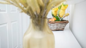 Una puerta blanca, una cesta de mimbre con flores amarillas y un florero con plantas secas.