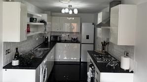 Una cocina moderna con gabinetes blancos, encimera negra, estufa a gas, horno integrado y pileta de acero inoxidable.