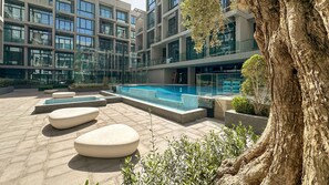 Ein moderner Poolbereich im Freien mit geometrischen Sitzgelegenheiten und einem großen Baum.