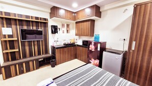 A compact kitchen with wooden cabinets, a microwave, a refrigerator, and a small sink. - Crescent Stays T Nagar (Hyderabad)