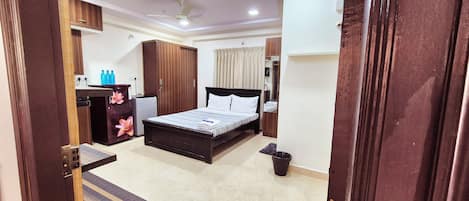 A bedroom with a bed, wardrobe, desk, and a small refrigerator.