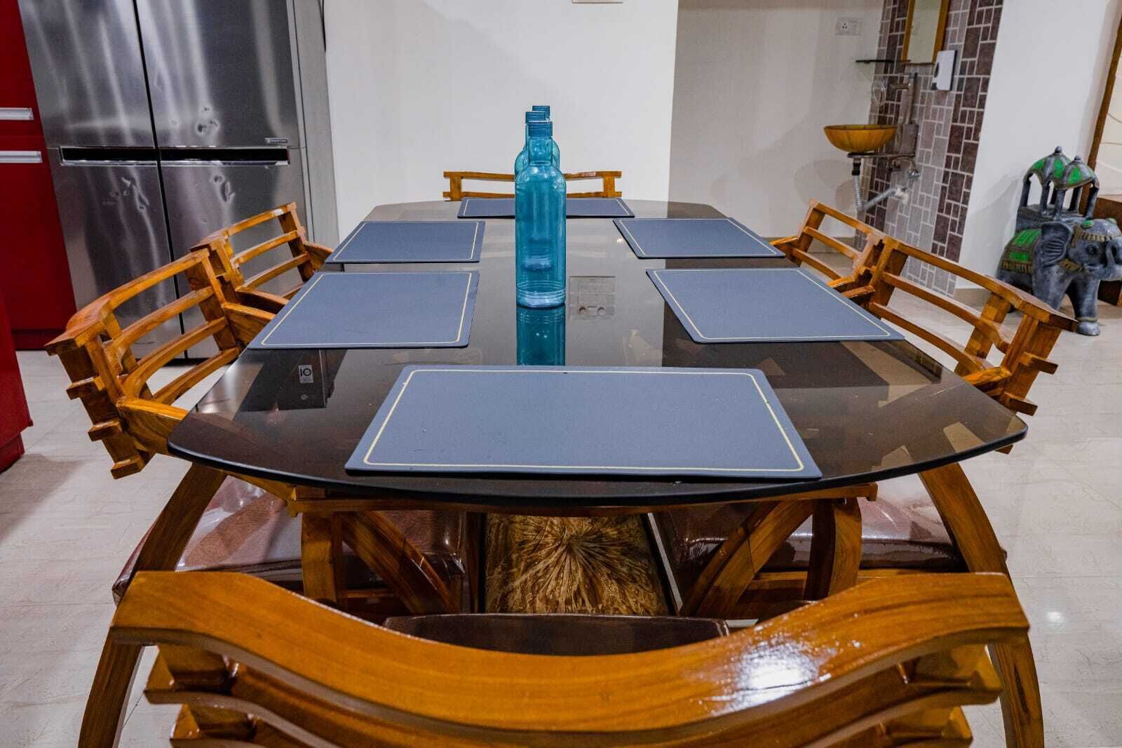 A round dining table with six chairs, a blue water bottle, and a stainless steel refrigerator in the background.