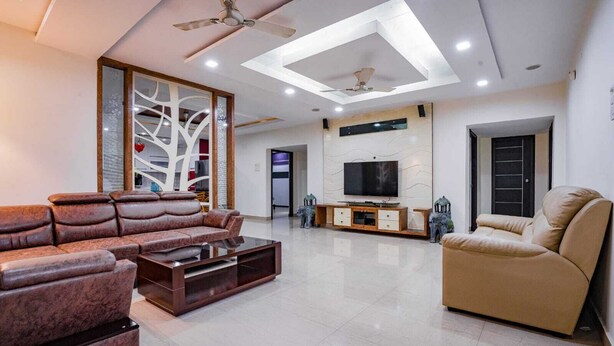 A modern living room with a sectional sofa, a coffee table, a TV, and a ceiling fan. - Crescent Stays T Nagar (Hyderabad)
