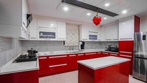 A modern kitchen with red and white cabinetry, a central island, and stainless steel appliances. - Crescent Stays T Nagar (Hyderabad)