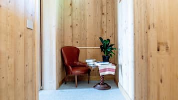 A small, cozy room with wooden walls, a red leather chair, a small table with a plant, and a few books.
