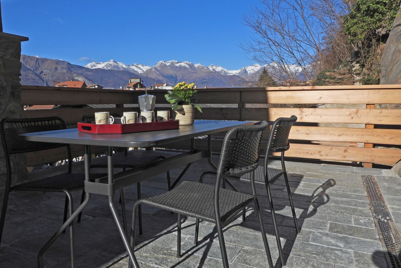 Patio esterno con tavolo e sedie, recinzione in legno e montagne sullo sfondo.