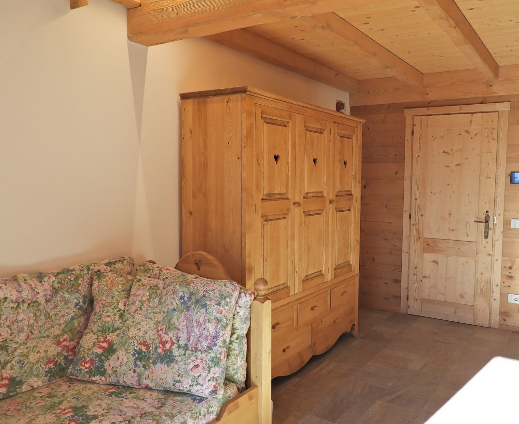 A room with a wooden wardrobe, a floral sofa, and a wooden door.