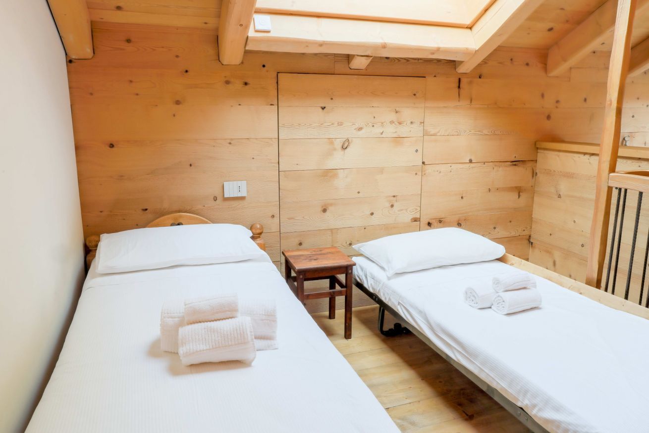 Una habitación pequeña y acogedora con dos camas individuales, paredes de madera, un tragaluz y una mesita de madera.