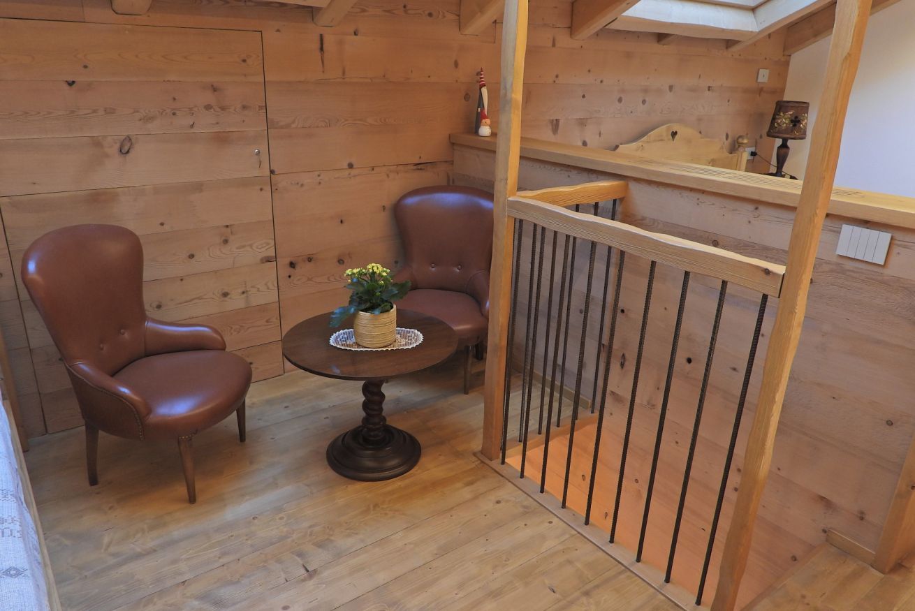 Une pièce chaleureuse aux murs et au plancher en bois, comprenant deux fauteuils en cuir, une petite table ronde agrémentée d’une plante et une rambarde en bois.