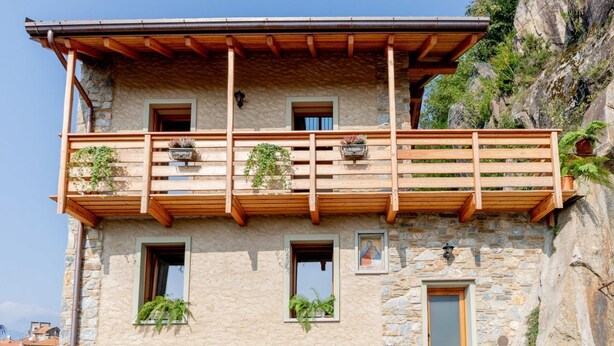 A stone building with a wooden balcony, multiple windows, and potted plants. - Green Chalet - Wonderfull terrace lake view - Jacuzzi and SPA  (Dervio)