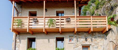 Un edificio de piedra con balcón de madera, varias ventanas y macetas con plantas.