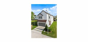 Ett envåningshus med ett garage, en röd dörr och en liten trädgård framför huset med en flaggstång och gräsmatta.