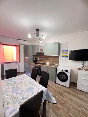 A compact kitchen with a washing machine, a dining table with chairs, and a TV mounted on the wall. - Gorgeous Open-Space (Bosa)