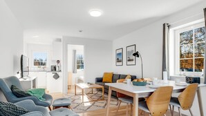 A modern living room with a sofa, chairs, a dining table, and a kitchen area visible through an open door. - "Ama" - 350m from the sea by Interhome (Læsø)