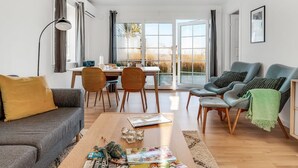 A modern living space with a sofa, coffee table, and chairs, a dining area with a table and chairs, and a large window with a view. - "Ama" - 350m from the sea by Interhome (Læsø)