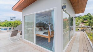 A modern room with a glass door leading to a balcony, a bed with a wooden frame, and a view of the surrounding area. - Modern 10BR ZipLine 3 Pools  V256 (Rawai)