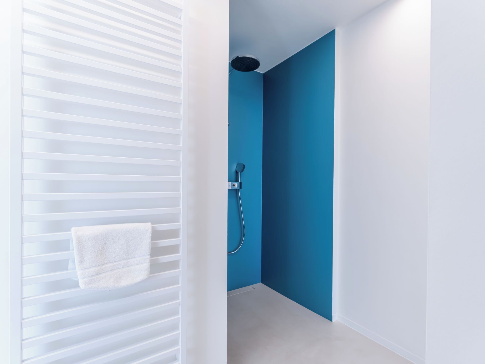 A modern bathroom with a blue accent wall, a white towel hanging on a rack, and a shower with a handheld showerhead.