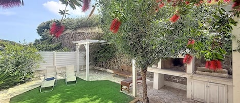 A patio area with a white pergola, a small tree, and a seating area with two chairs.