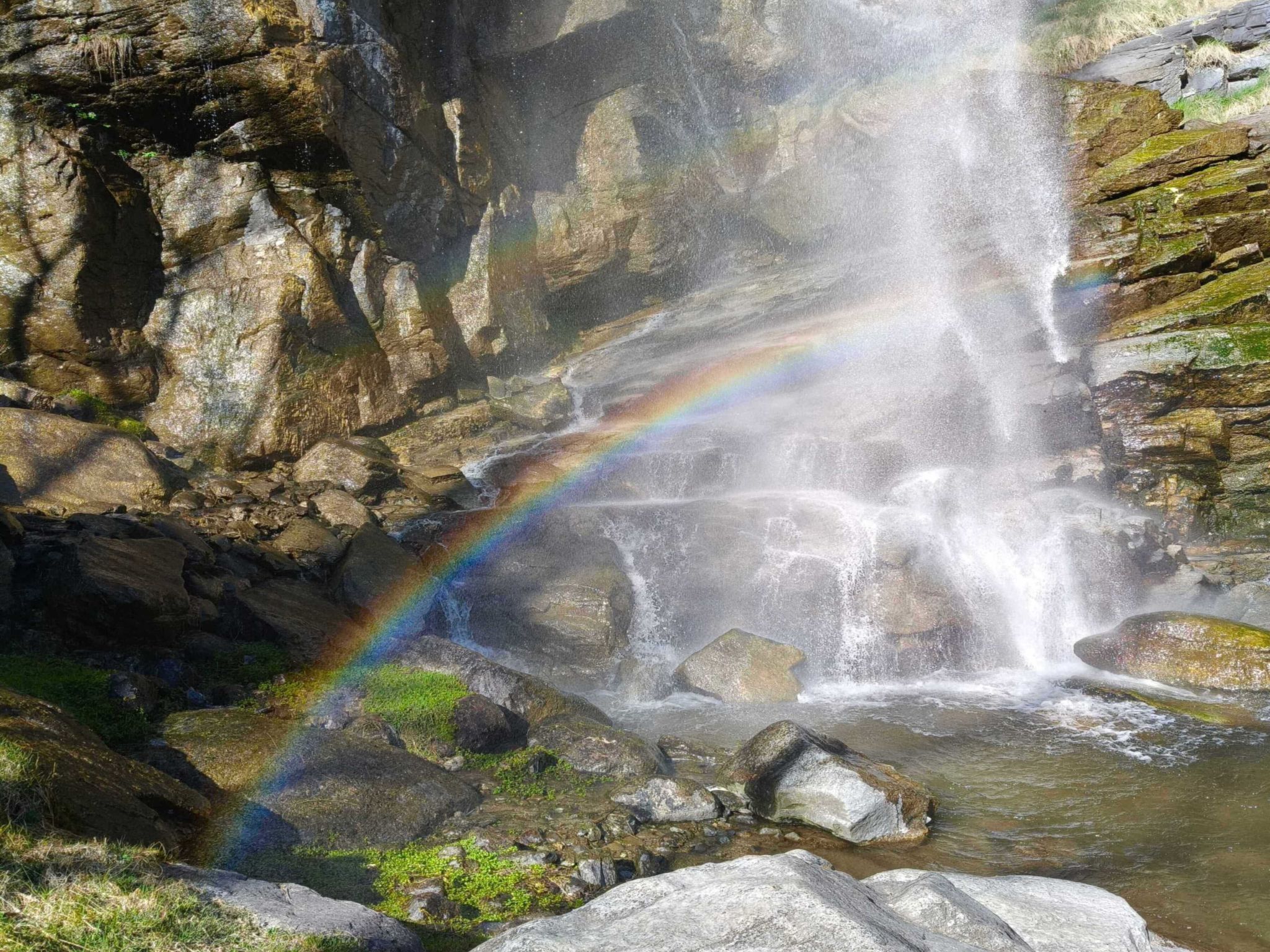 A waterfall with a rainbow, surrounded by rocks and greenery.