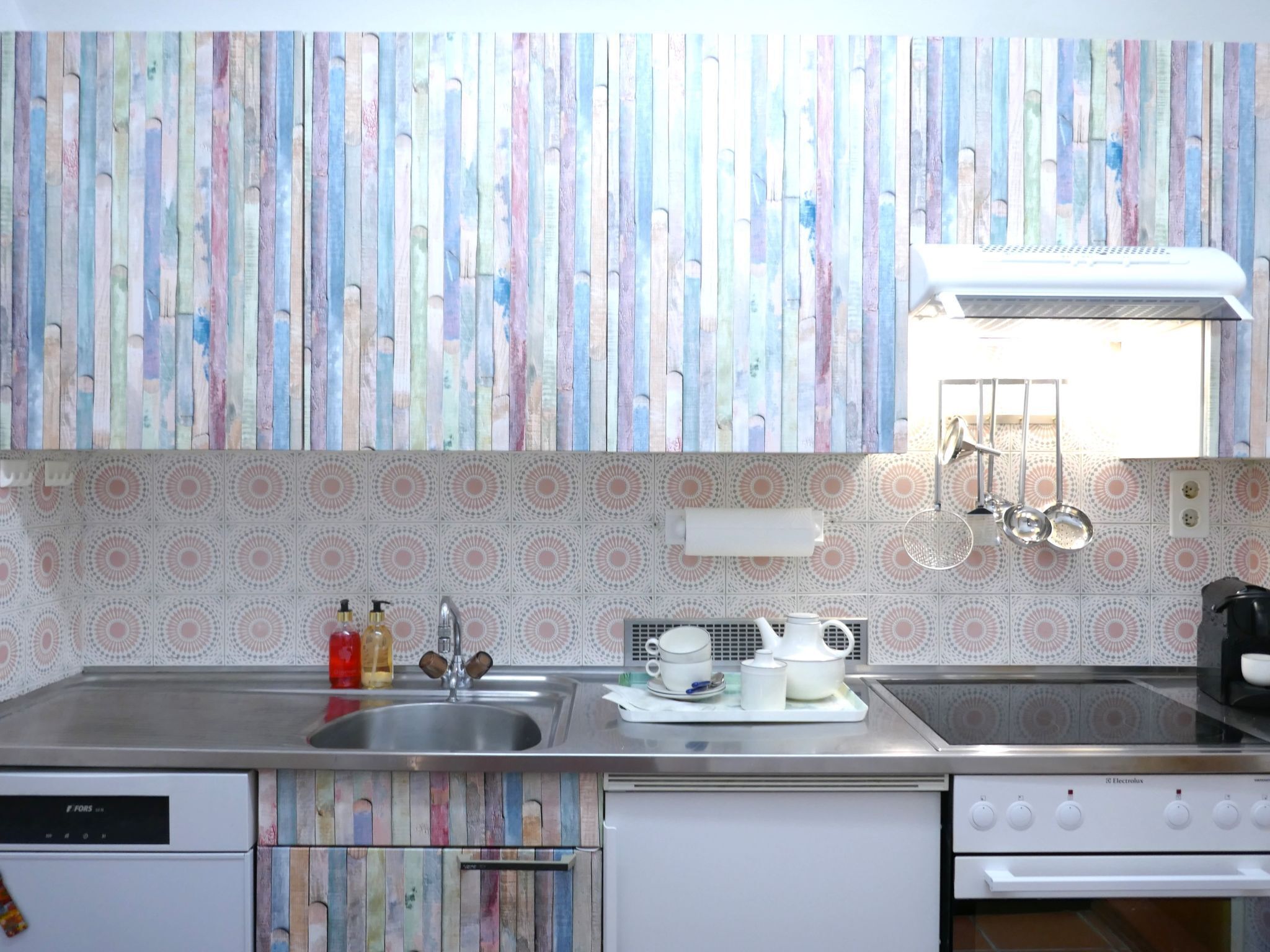 A kitchen with a colorful vertical wooden panel backsplash, a stainless steel sink, and a white stove.