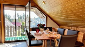 Ein Essbereich mit Holztisch, gedeckt für zwei Personen, einer Bank und Blick auf einen umzäunten Garten.