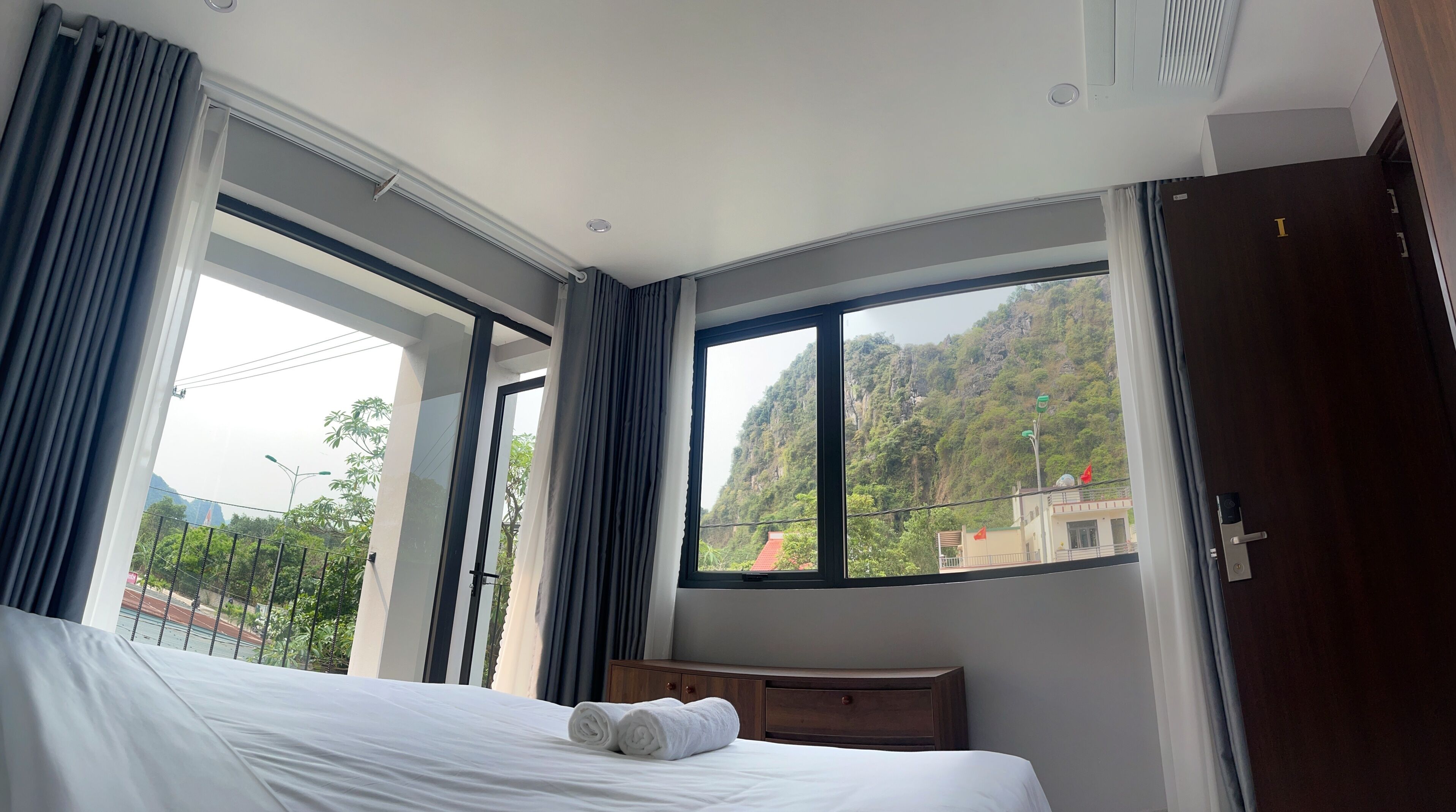 A hotel room with a large bed, a wooden headboard, and a view of a mountainous landscape through large windows.