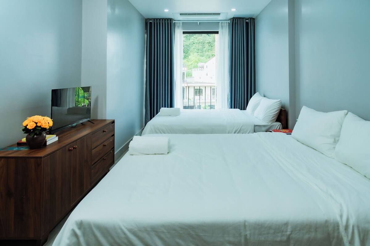 Ein Hotelzimmer mit zwei Betten, einem Fernseher auf einer Holzkommode und einem Fenster mit Vorhängen.