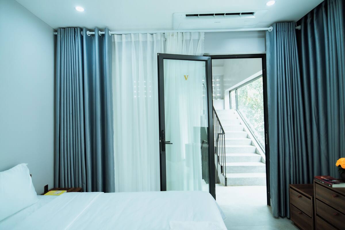 Ein modernes Hotelzimmer mit einem Bett, einem Nachttisch, einer Kommode und einer Glastür zu einer Treppe.