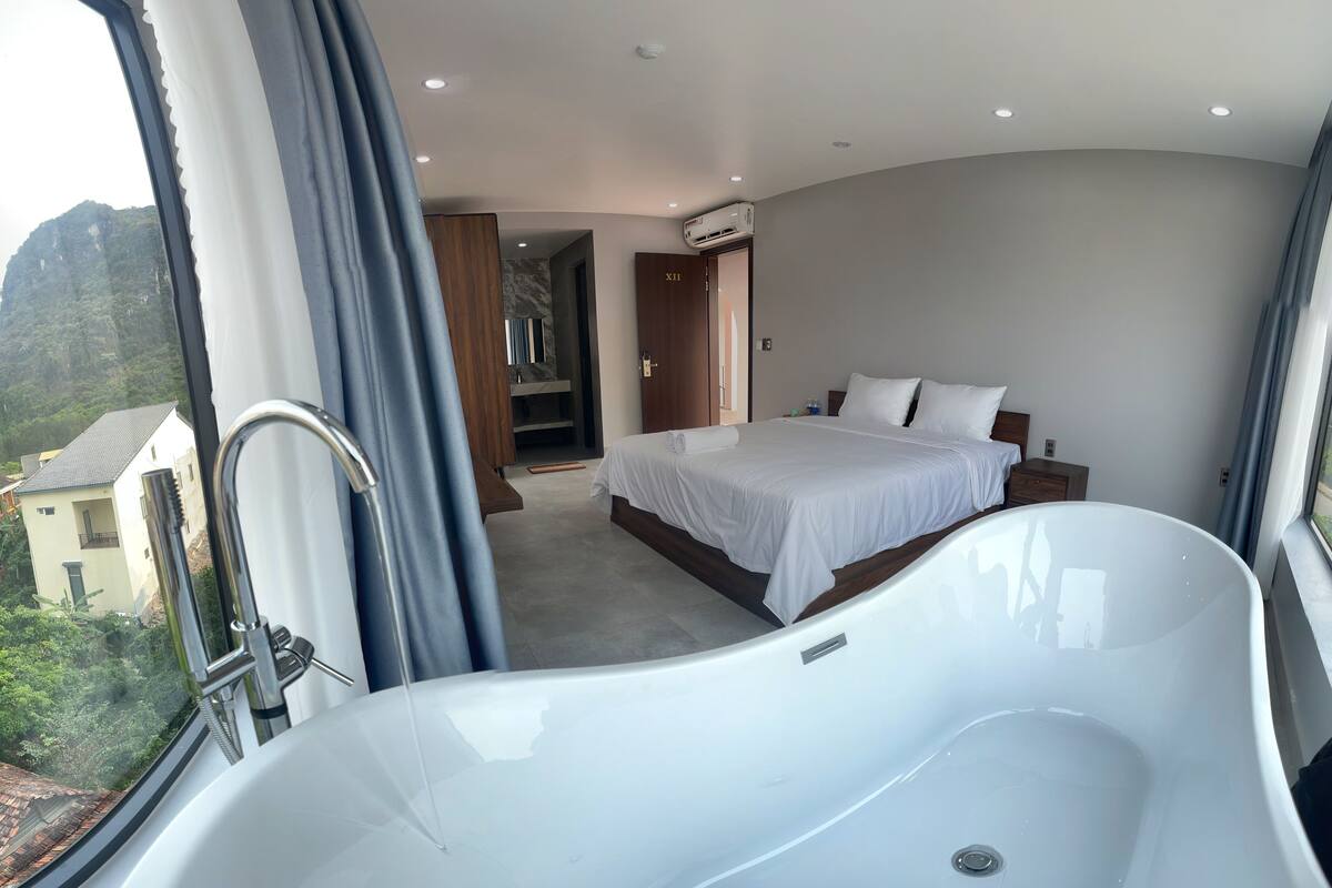 Ein modernes Hotelzimmer mit einer großen Badewanne, einem ordentlich bezogenen Bett und Blick auf die Berge.
