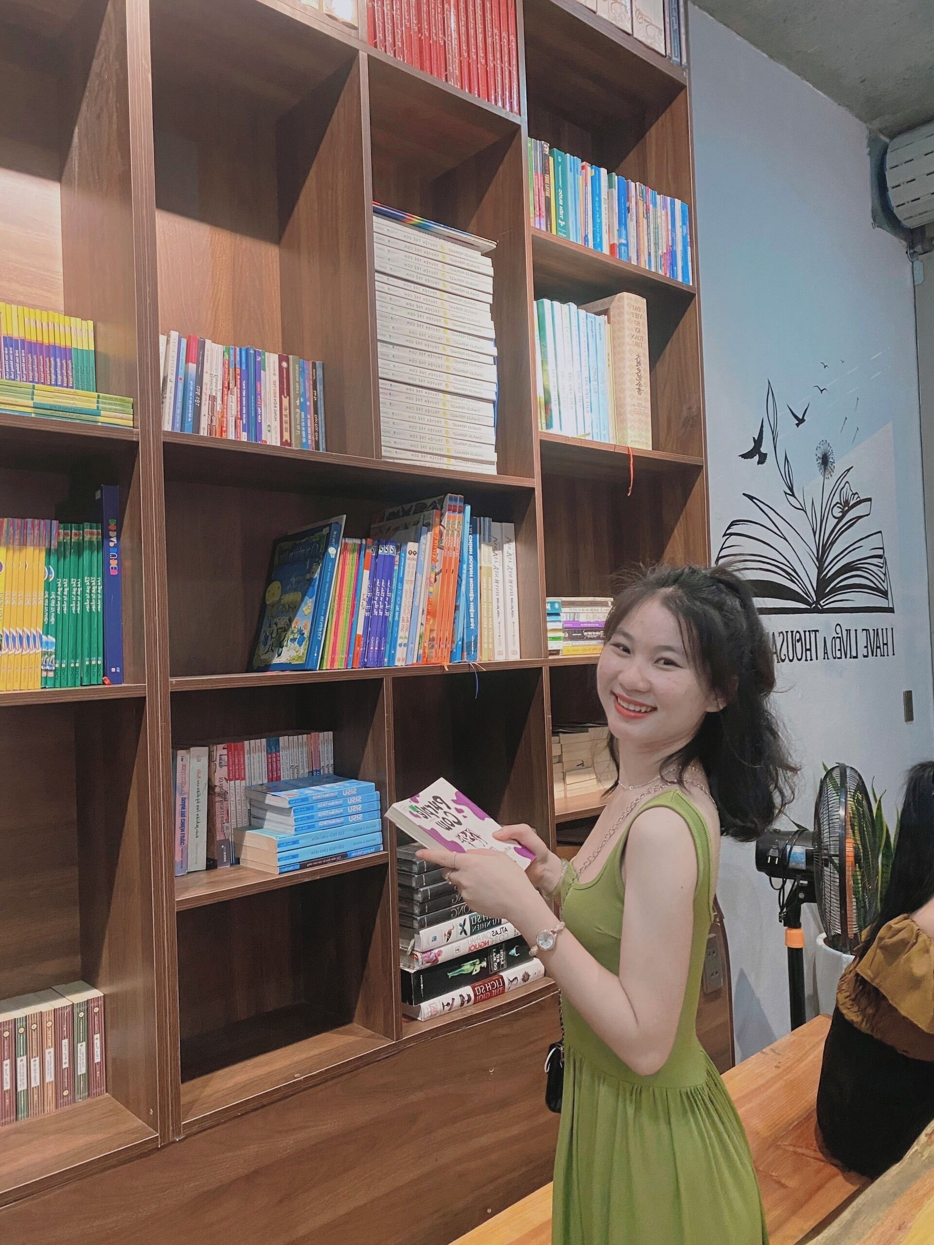 A woman holding a book in a library with wooden bookshelves filled with various books.