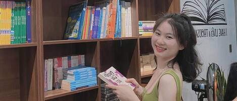 A woman holding a book in a library with wooden bookshelves filled with various books.