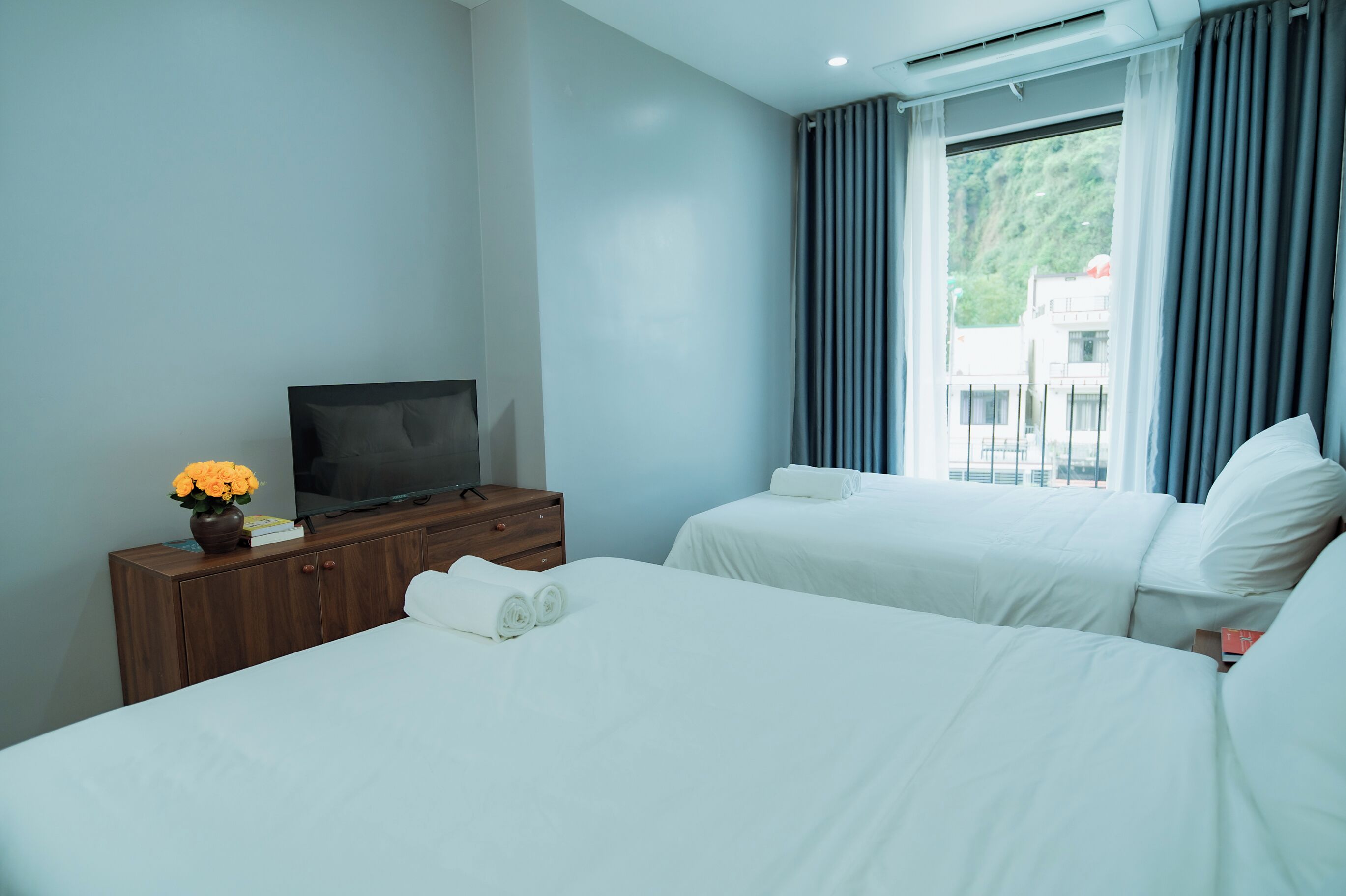 A hotel room with two beds, a TV on a wooden dresser, and a window with curtains.